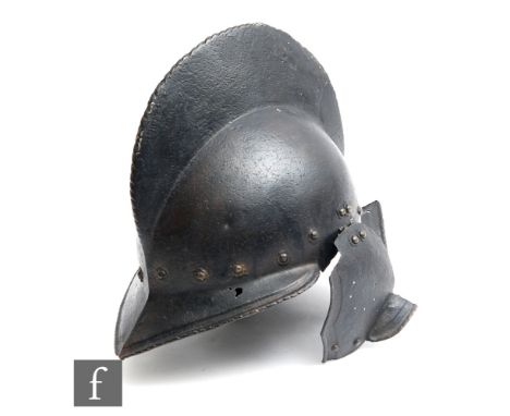 A Burgonet iron helmet with pronounced peak and tail and side flap hinged ear coverings and prominent comb, above a border of