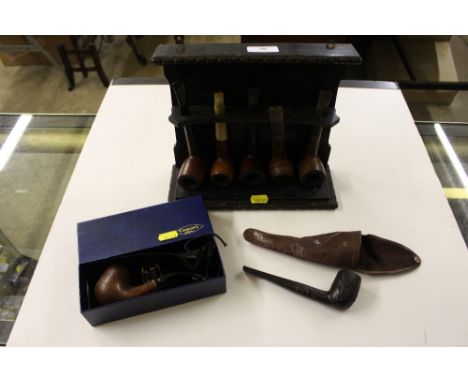 An oak pipe rack with five various pipes; together with a Dunhill pipe in leather case; and a Comoys of London pipe in box