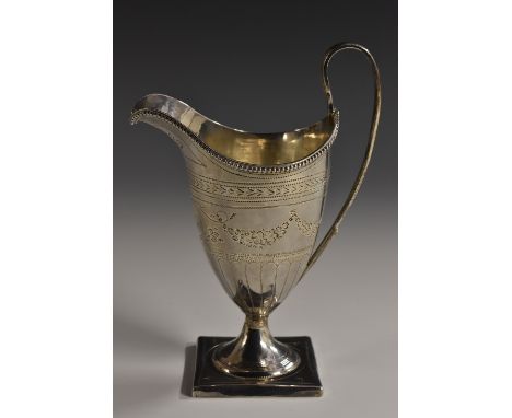 A George III silver helmet shaped cream jug, bright-cut engraved with swags and wriggle-work, beaded rim, lofty scroll handle