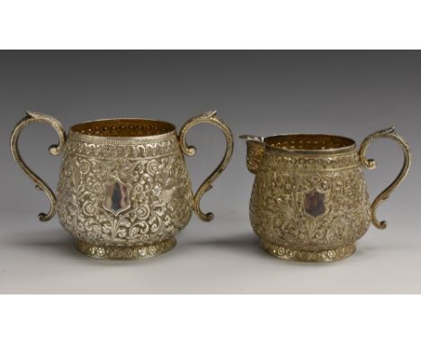 An Indian silver cream jug and sugar basin, of heavy gauge, profusely chased with stylised animals amongst dense scrolling fo