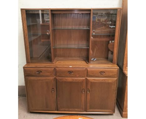 A modern Ercol full height side cabinet in medium elm, the top with 2 glazed cupboards and open shelves, the base with 3 cupb