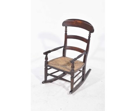 A 19th Century stained hardwood child's rush seat rocking chairWith a ladder back above an envelope rush seat flanked by slen