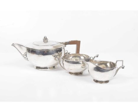 An Art Nouveau style silver three piece tea serviceOf squat circular form, with spot hammered decoration, raised on a circula