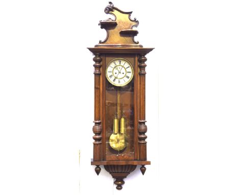A late 19th Century mahogany cased Vienna wall clock The carved upper pediment extending to a column and glazed door revealin