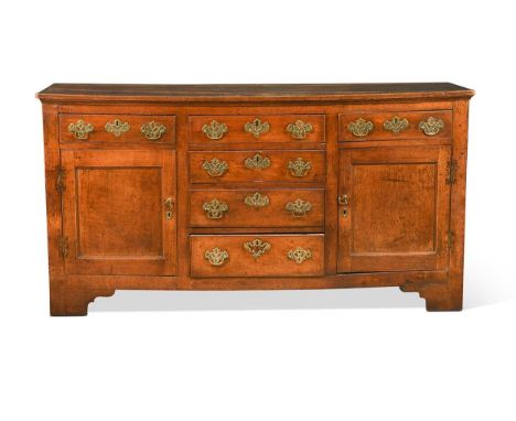 A George III elm and fruitwood dresser base, the arrangement of seven drawers flanked by two panelled cupboard doors on brack