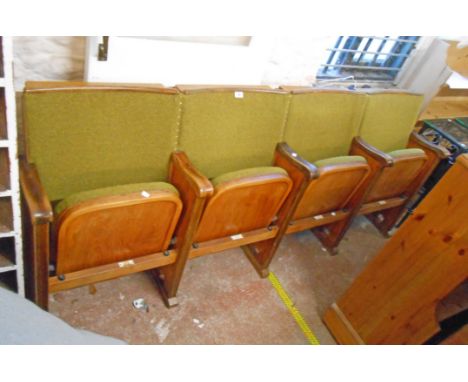 A row of four vintage cinema seats with polished wood part show frames, moulded arm rests and green upholstery, with pop-up t