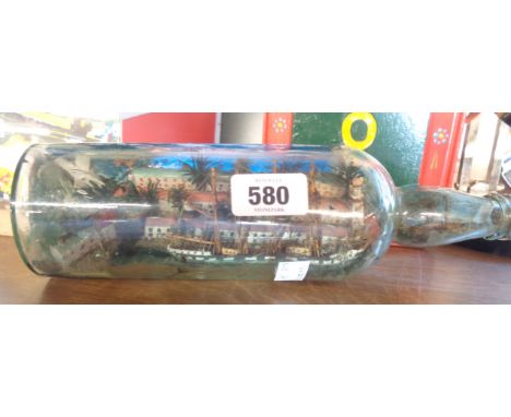 A vintage ship in a bottle diorama depicting a coastal town with windmill, church and lighthouse, and a clipper being towed b