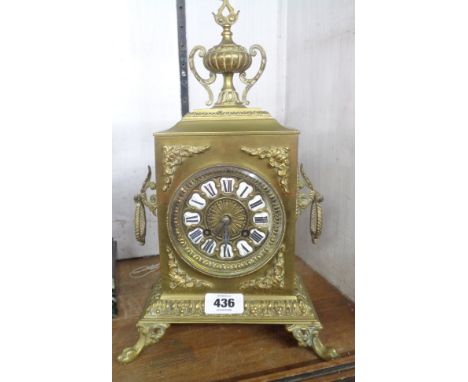 A late Victorian ornate cast brass cased mantle clock with urn pattern finial to top, flanking loop handles and enamelled rom