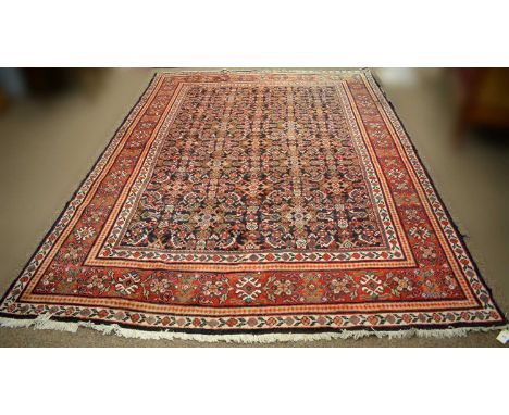 An Eastern bordered carpet, decorated with a rich field of geometric and foliate designs in blue, orange and red, 315 x 220cm