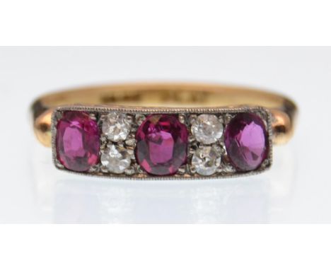 An 18ct gold ruby and diamond ring. The ring being set with three oval cut rubies interspaced with four old cut diamonds with