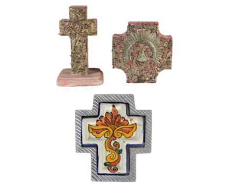 Two wooden sculptural objects decorated with milagros. The third cross is a ceramic wall hanging in a metal frame, as is cond