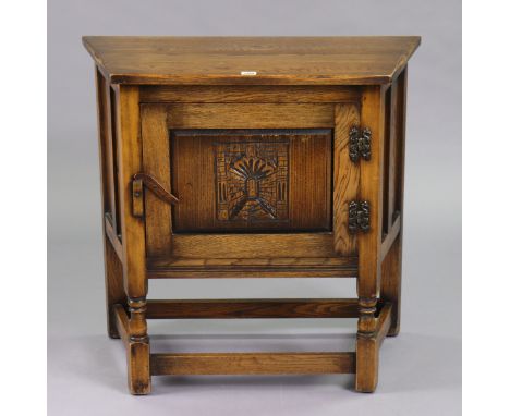 A small oak side cabinet with canted sides, enclosed by a carved panel door, &amp; on turned supports with plain stretchers, 