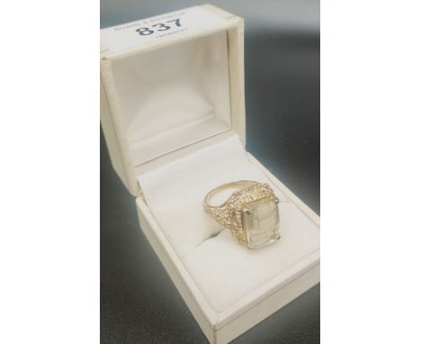 9ct yellow gold ornate ladies ring fitted with a pale blue Emerald cut stone. [Ring size N] [5.53Grams] 