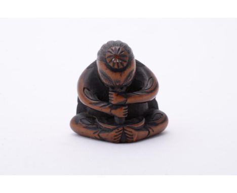 A Wood Netsuke carved in the form of a Tengu, seated cross-legged as it uses its long nose to stir a bowl of moxa gripped in 