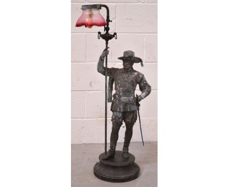 A freestanding spelter gas lamp in the form of a cavalier, raised on plinth base with cranberry shade, height 95cm.