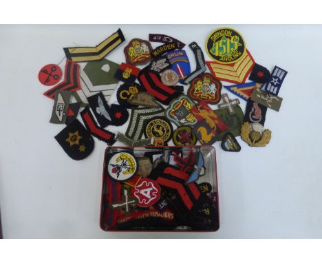 A tin of British Army cloth rank and regimental badges.