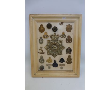 A framed display of 21 military cap badges including a Royal Lancaster Regiment 1st Volunteer Battalion helmet plate.