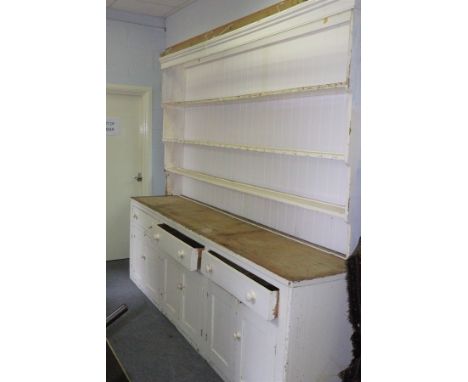 A large white painted pine dresser base, fitted three drawers above cupboards with a later rack of shelves above, the base 28