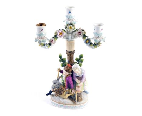 A Dresden porcelain candelabrum, modelled in the form of a young man and lady with sledge, etc., 32cm high. (AF)