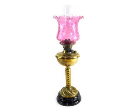 An early 20thC brass oil lamp, with cranberry glass shade, plain glass chimney, and raised brass reservoir, on turned stem an