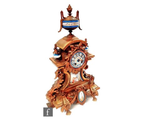 A late 19th Century French gilt metal mantel clock inset with Sevres style panels, surmounted by an urn above the enameled di