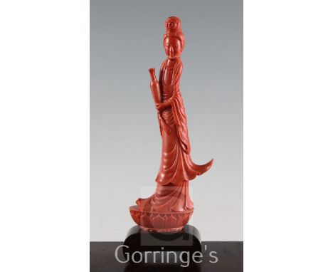 A large Chinese coral figure of Guanyin, holding a vase and a scroll and standing on a lotus lappeted base, 27.7cm incl. wood
