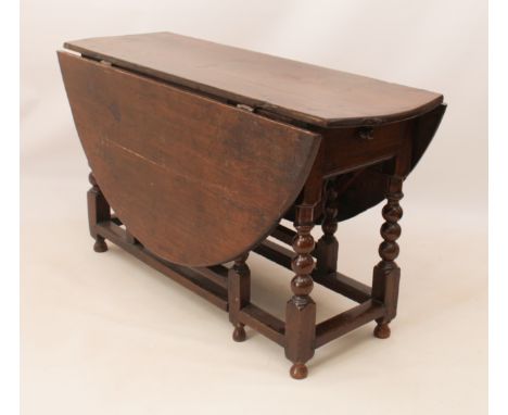 An early 18th century oak gateleg dining table - the oval dropflap top over a single end drawer (later lined with baize), rai