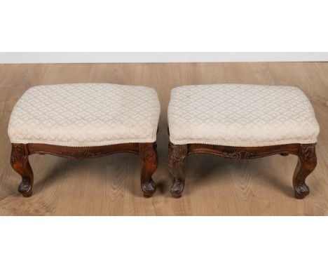 A pair of carved wooden footstools With overstuffed cream upholstery raised on cabriole legs.Each 42cm wide x 29cm deep x 25c