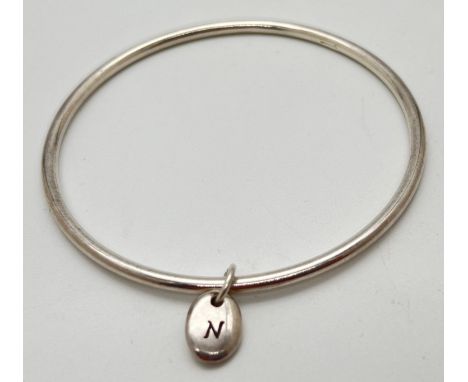A modern silver thin bangle with oval dangle charm engraved with initial N. Hallmarked Birmingham 2015 to inside of bangle. A