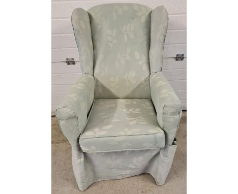 A vintage wooden framed wing back armchair, reupholstered with green foliate design material. 