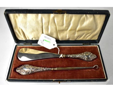 A George V hallmarked silver cased set of button hook and shoehorn, the handles with repoussé Rococo-style decoration, J&amp;