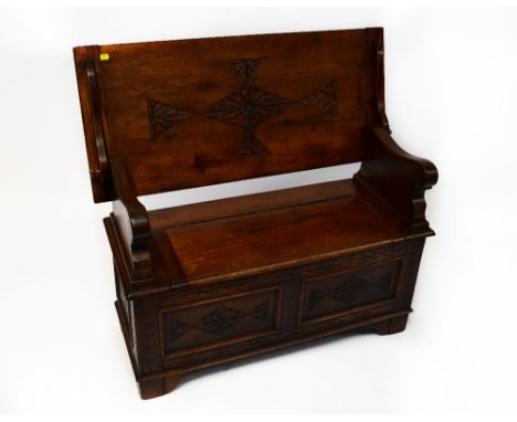 A 20th century reproduction oak monks bench, with carved table top and underside, pegged and metal hinges, solid curved armre