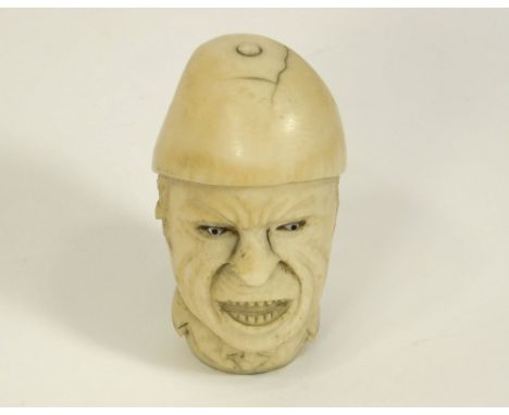 CANE FINIAL. An antique, carved ivory cane finial, a grotesque man's head with inset glass eyes, & wearing possibly a French 