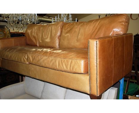 A contemporary tan leather and brass studded two-piece suite, comprising three-seater sofa and single armchair, sofa w.223cm
