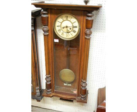 A circa 1900 Vienna walnut cased drop trunk wall clock, the enamelled circular dial with twin winding holes, pendulum and win