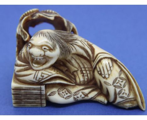 Ivory carved netsuke in the form of a figure reclining with a floral background, L: 55 mm, unsigned. Fine crack to top of hea
