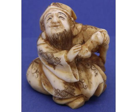 Ivory carved netsuke in the form of a bearded man seated on a cushion holding a staff, H: 40 mm, signed to base P&amp;P Group