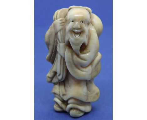 Ivory carved netsuke in the form of a smiling god carrying a sack, H: 47 mm, signed to back. Age crack to base, otherwise goo