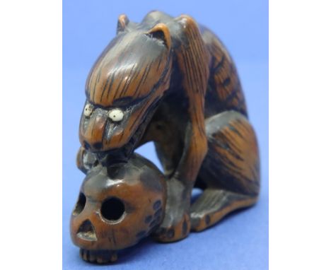 Carved boxwood netsuke in the form of a wolf with ivory eyes resting on a skull, H: 40 mm, unsigned. P&amp;P Group 1 (£14+VAT