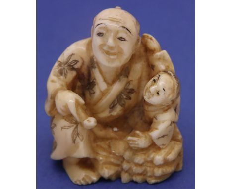 Ivory carved netsuke in the form of a man holding a pipe with a child, H: 36 mm, signed to base. P&amp;P Group 1 (£14+VAT for