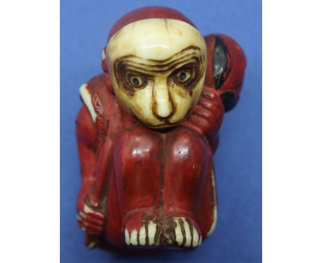 Ivory carved netsuke in the form of a red seated monkey holding a fruit, H: 36 mm, unsigned. Netsukes holes show some wear, m