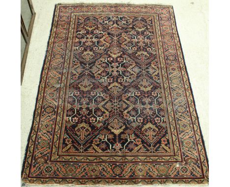 A Persian style carpet the central panel set with repeating diamond medallions on a dark blue ground with stylised foliate de