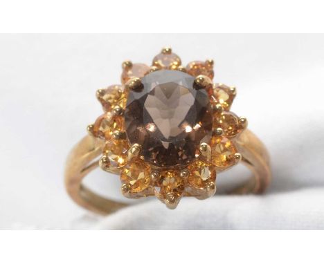 A smokey quartz and citrine cluster ring, the central oval facet-cut smokey quartz surrounded by twelve circular facet-cut ci