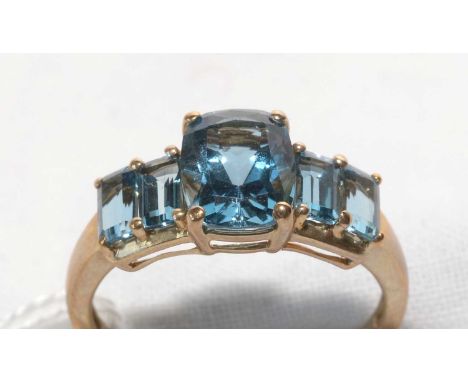 A blue topaz ring, the central oval scissor-cut topaz flanked by rectangular step-cut topaz to each shoulder, on 9ct. gold sh