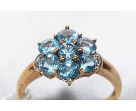 A blue topaz cluster ring, the seven uniform circular facet-cut topaz flanked by diamond set shoulders, on 9ct. yellow gold s