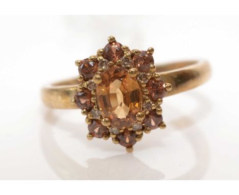 A brown zircon cluster ring, the central oval facet-cut zircon surrounded by eight circular zircons, on 9ct. yellow gold shan