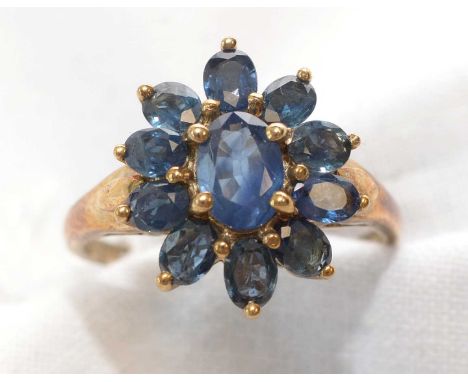 A Than sapphire cluster ring, the central oval facet-cut sapphire surrounded by ten smaller oval facet-cut sapphires, on 9ct.