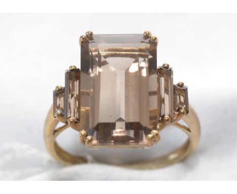 A smokey quartz ring, the principal rectangular step-cut smokey quartz flanked by two smaller quartz stones to each shoulder,