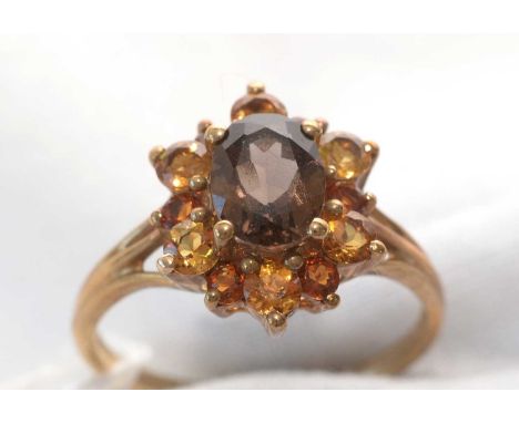 A smokey quartz and citrine cluster ring, the central oval facet-cut smokey quartz surround by bi-coloured citrine stones, on