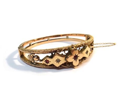 A 9ct gold, diamond and red gem set oval hinged bangle, with scroll pierced, beaded and openwork decoration, on a snap clasp,